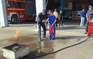 Eine Schülerin löscht angeleitet von einem Feuerwehrmann ein Feuer mit einem Feuerlöscher