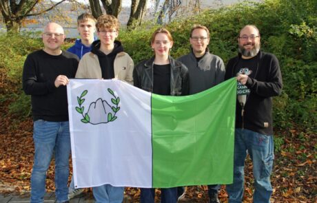 Der Präsident, die Vizepräsidentin, der Oppositionsführer sowie Lehrer aus dem Organisationsteam, stellen die Flagge von Trimon vor.